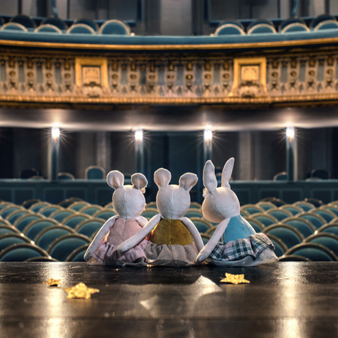 Drie Moulin Roty pluchen dieren, waaronder een konijn, zitten van achteren gezien op een podium in een theater.