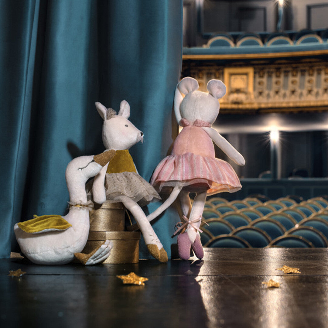 Een Moulin Roty knuffelmuis in roze ballerina-outfit en een knuffelgans staan op een podium.