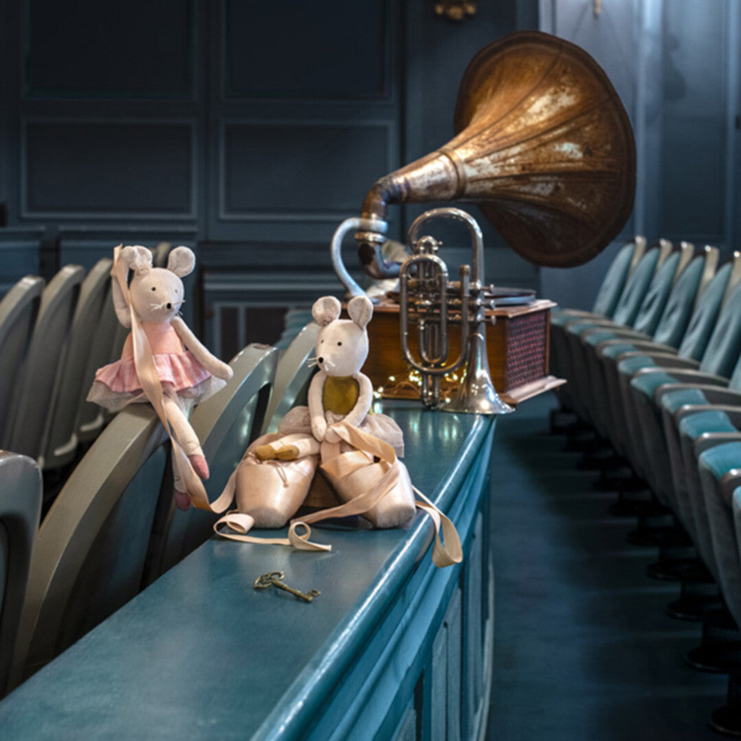 Twee Moulin Roty knuffelmuizen zitten naast balletschoenen op een leuning in een theaterzaal met een grammofoon.
