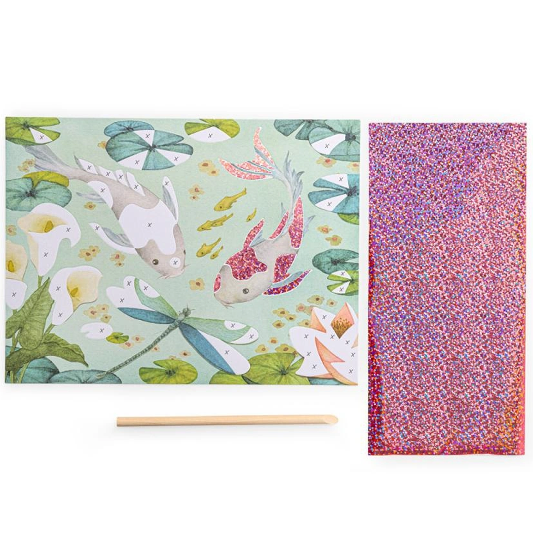 Een fantasy board van de knutselset met twee koi vissen en waterlelies, naast een glitterfolie en houten stokje.