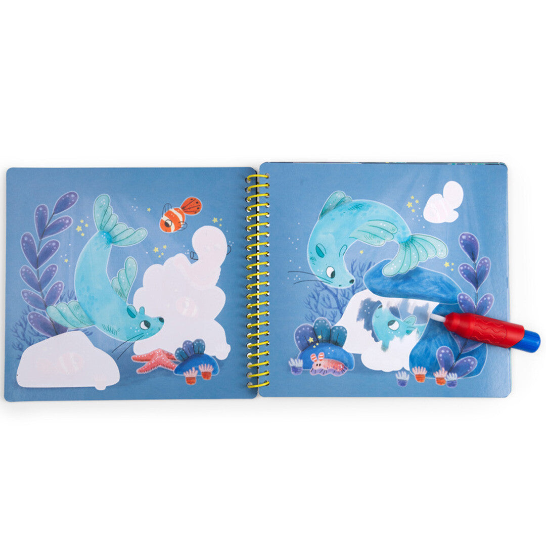 Open magisch schilderboek met een rode kwast die een wit vlak op een onderwaterpagina inkleurt, waardoor een zeehond zichtbaar wordt.
