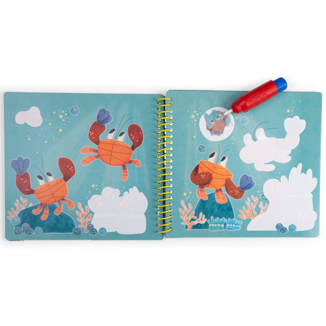 Open magisch schilderboek met twee pagina's die oranje krabben in een onderwaterlandschap tonen, met een rode kwast die een deel inkleurt.