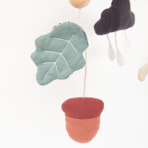 Detail van de Moulin Roty babymobiel met een houten arm, een groen stoffen blad en een rood stoffen eikel.