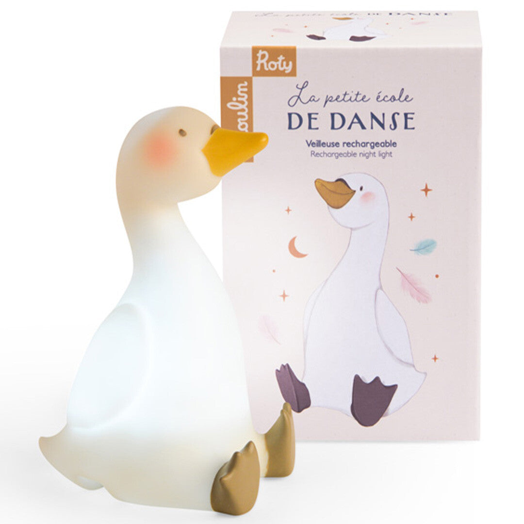 Moulin Roty nachtlampje in de vorm van een zwaan, lichtgevend, naast de productverpakking.