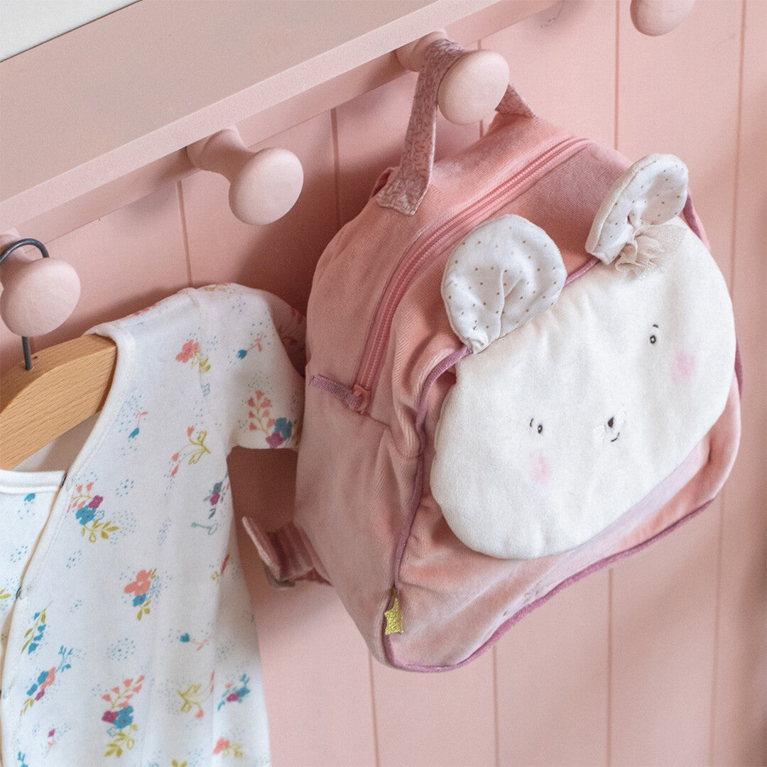 Moulin Roty roze peuterrugzak met muisgezicht hangt aan een roze kapstok naast een romper.