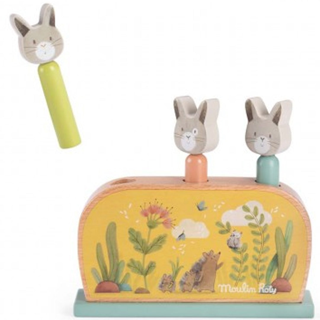 Moulin Roty houten pop-up spel voor baby's met twee konijnen in de gaten en één konijn los erboven, op een gele basis met bosdieren en planten.