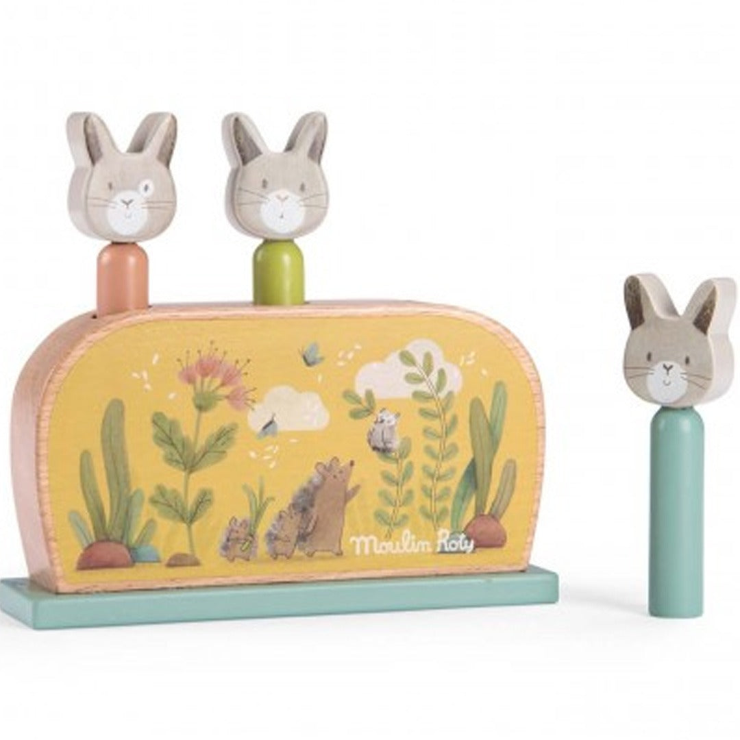 Moulin Roty houten pop-up spel voor baby's met twee konijnen in de gaten en één konijn ernaast, op een gele basis met bosdieren en planten.