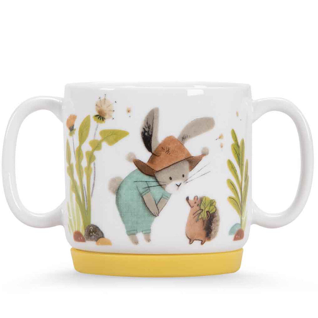 Witte porseleinen kindermok met twee handvatten en een gele basis, met een konijn en een egel tussen bloemen.