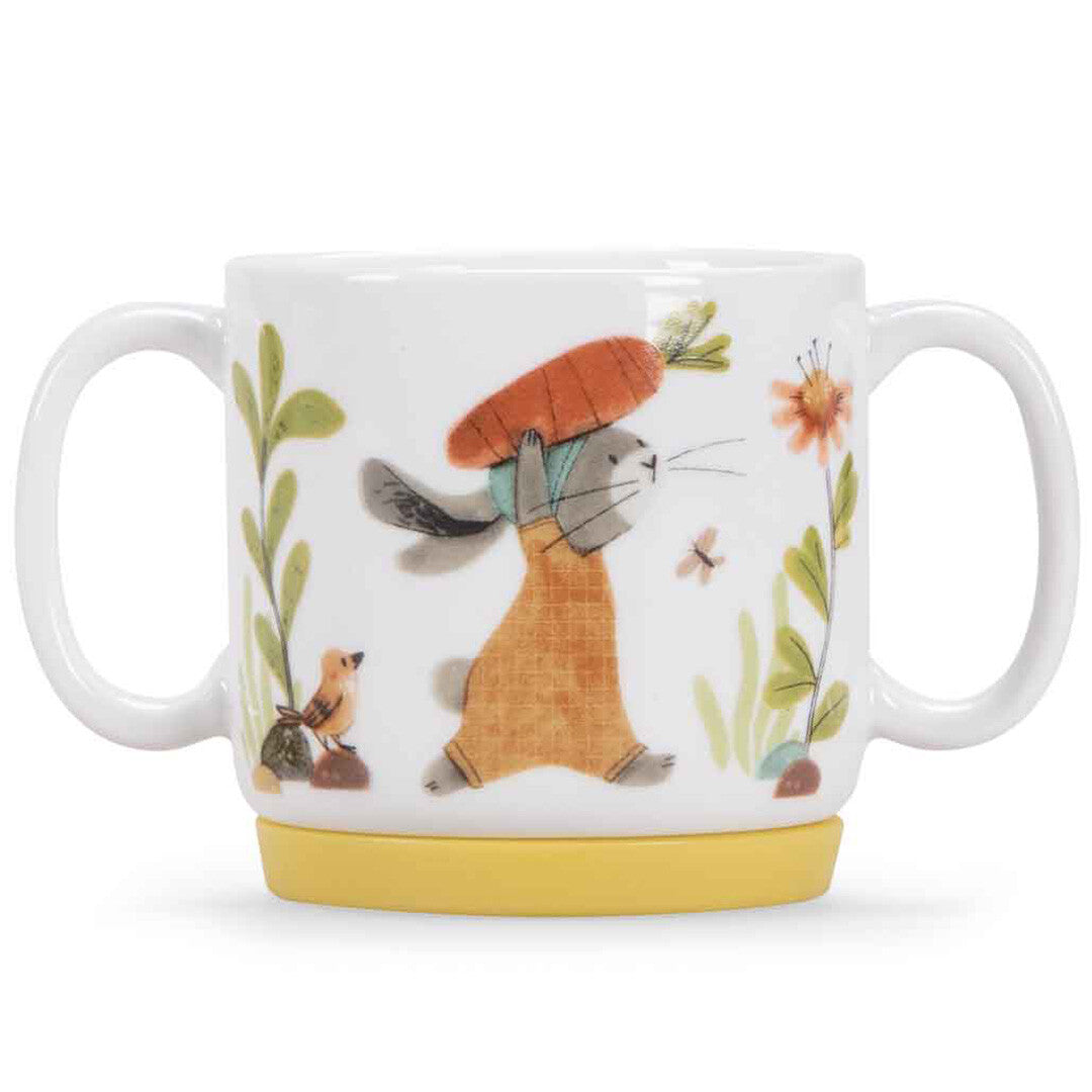 Witte porseleinen kindermok met twee handvatten en een gele basis, met een konijn dat een wortel draagt.