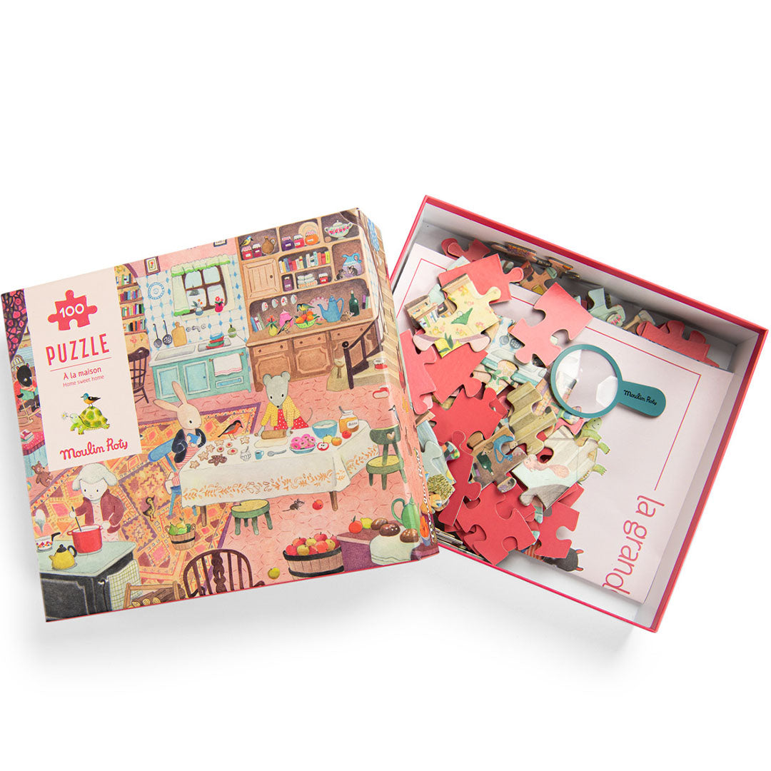 Open Moulin Roty puzzeldoos met losse puzzelstukjes en een vergrootglas, naast de deksel met de illustratie van dieren in een keuken.