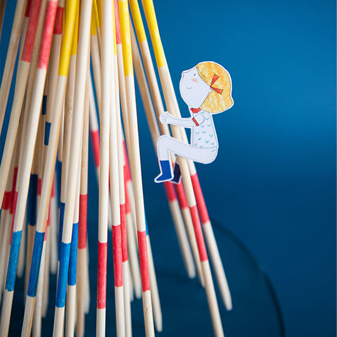Detailopname van het Moulin Roty reuze mikado behendigheidsspel met een papieren figuur van een meisje tussen de stokjes.