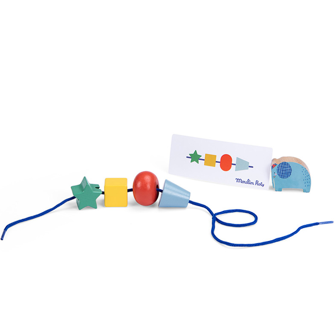 Een blauw rijgkoord met houten Moulin Roty kralen in de vorm van een ster, kubus, bal en kegel, naast een patroonkaart en een olifantje.