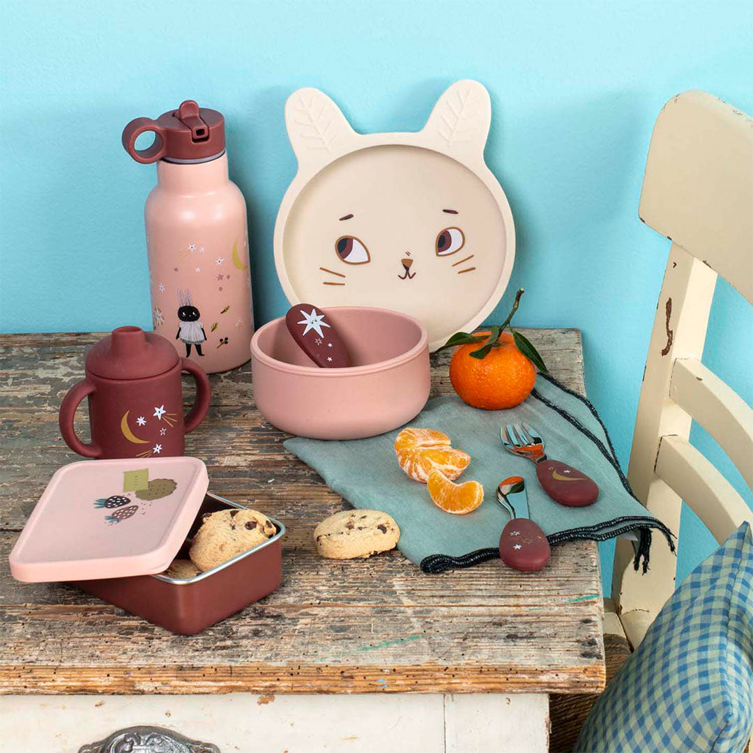 Moulin Roty kinder eetset met snackdoosje, drinkfles, bord, kom en bestek op een houten tafel.