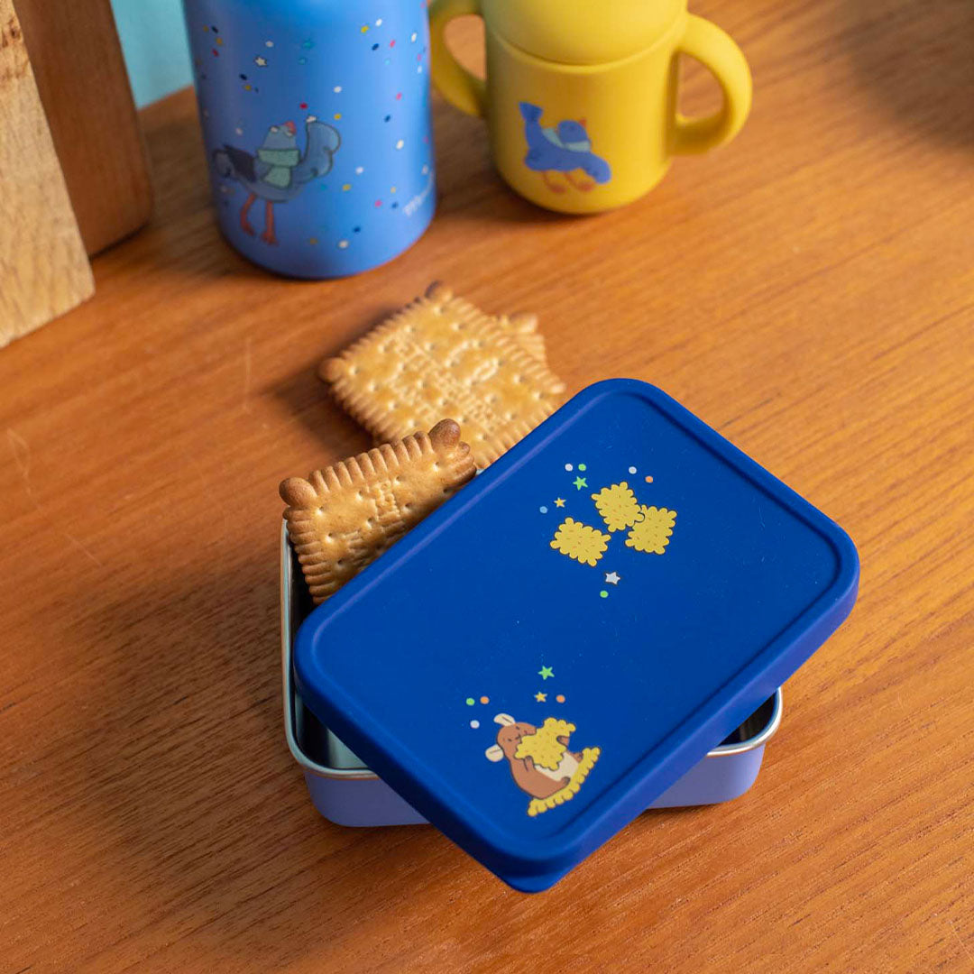 Open blauw kinder snackdoosje met koekjes en de deksel ernaast, op een houten tafel.