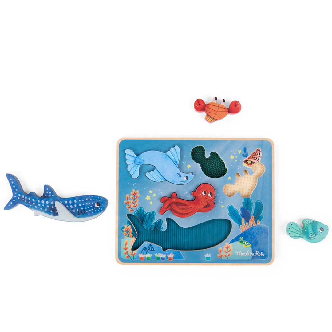 Moulin Roty houten sensorische puzzel voor peuters met onderwaterdieren, waarbij enkele puzzelstukken naast het bord liggen.