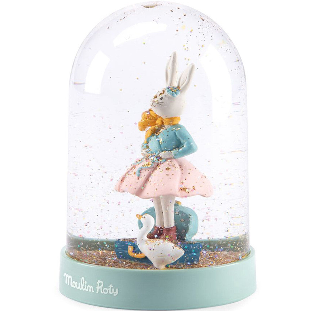 Moulin Roty sneeuwbol met konijn Victorine, een eendje en een koffer, schuin gefotografeerd.