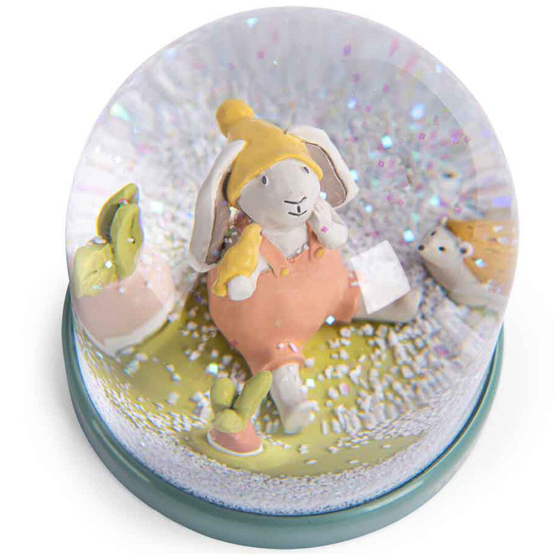 Bovenaanzicht van de Moulin Roty sneeuwbol met een konijntje, een vogel, een egel en een wortel, met dwarrelende glitter.
