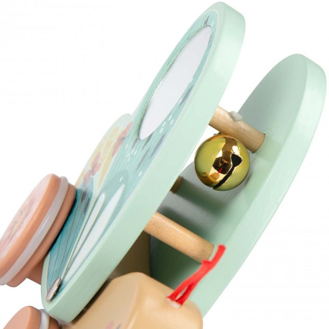Detailopname van de Moulin Roty houten trekfiguur vlinder, met een gouden bel zichtbaar tussen de openstaande groene vleugels.