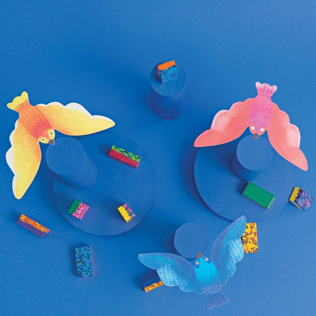 Moulin Roty meerkleurige waskrijtjes op een blauwe ondergrond met decoratieve vogeluitsparingen.