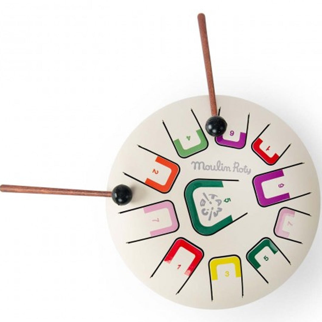 Moulin Roty tongdrum muziekspeelgoed met veelkleurige toetsen en twee drumstokjes, van bovenaf gefotografeerd.