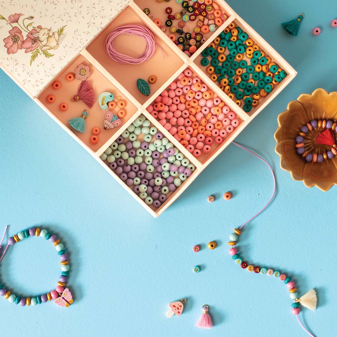Bovenaanzicht van een open houten kralenset met diverse gekleurde kralen, touw en gemaakte armbandjes.