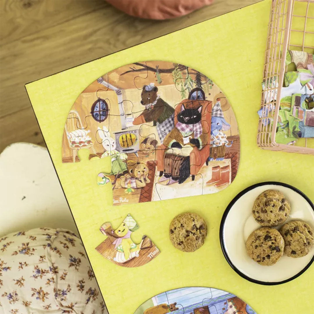 Gelegde Moulin Roty legpuzzel met dieren in een huiselijke setting, naast een bord met koekjes.