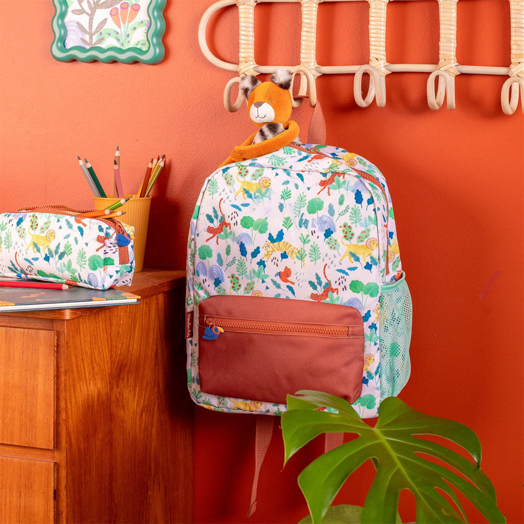 Moulin Roty kleuterrugzak met jungle dieren en bladeren patroon, hangend aan een haak naast een bijpassende etui.