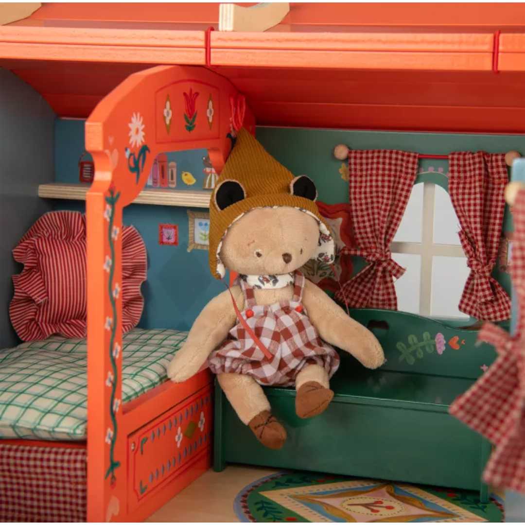 Detail van het interieur van de Moulin Roty houten stacaravan poppenhuis met een beer op de bank en een bed.