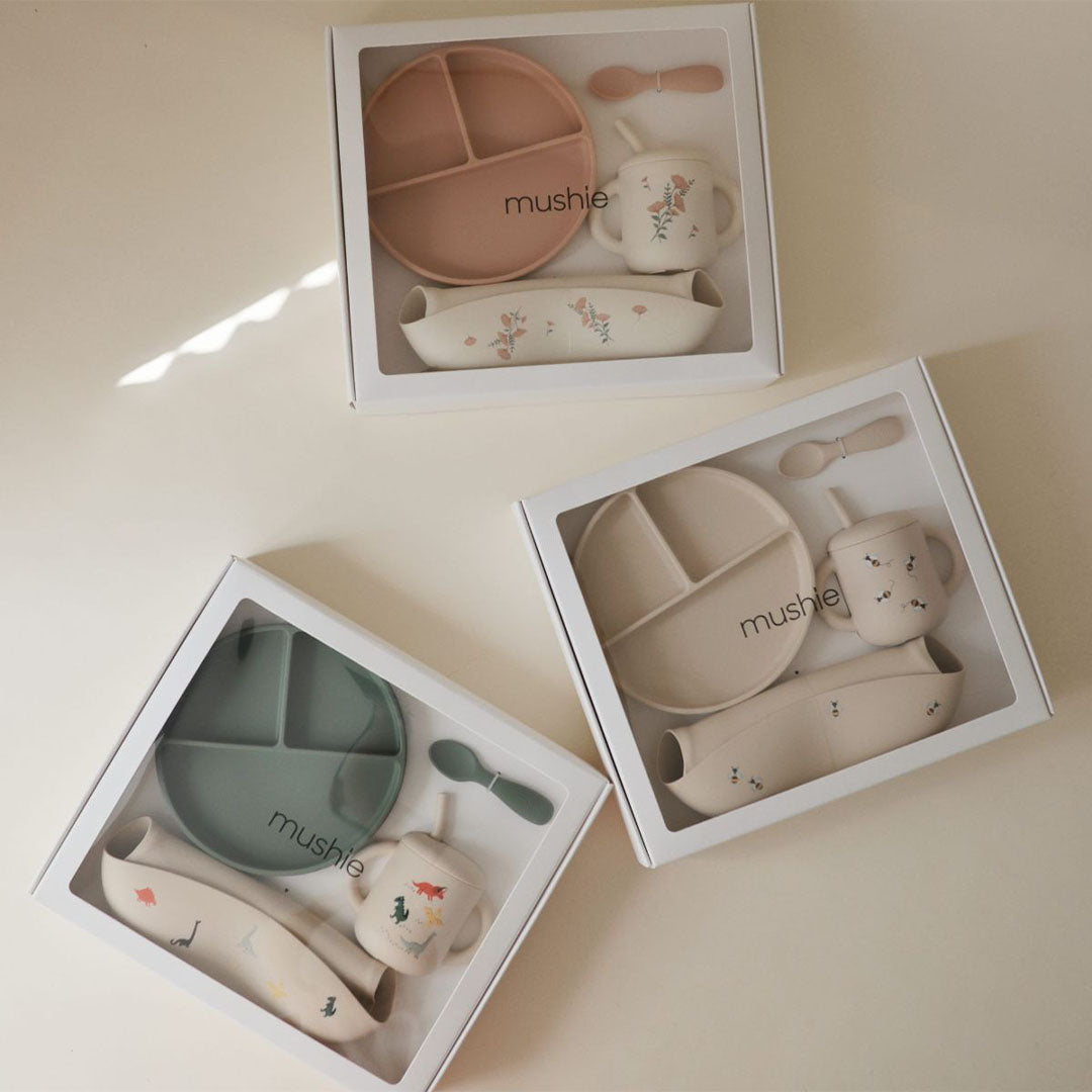 Drie Mushie siliconen voedingssets voor baby's in geschenkverpakkingen, met dino- en bloemenpatronen.