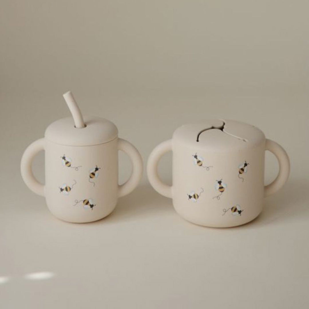 Twee mushie siliconen bekers voor baby's met bijenpatroon, een snackbeker en een drinkbeker met rietje.