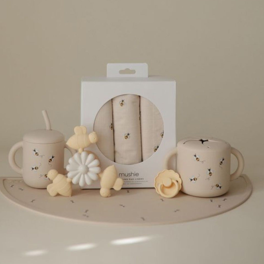 Een collectie mushie babyproducten met bijenpatroon, waaronder een snackbeker, drinkbeker, doekjes en speelgoed.