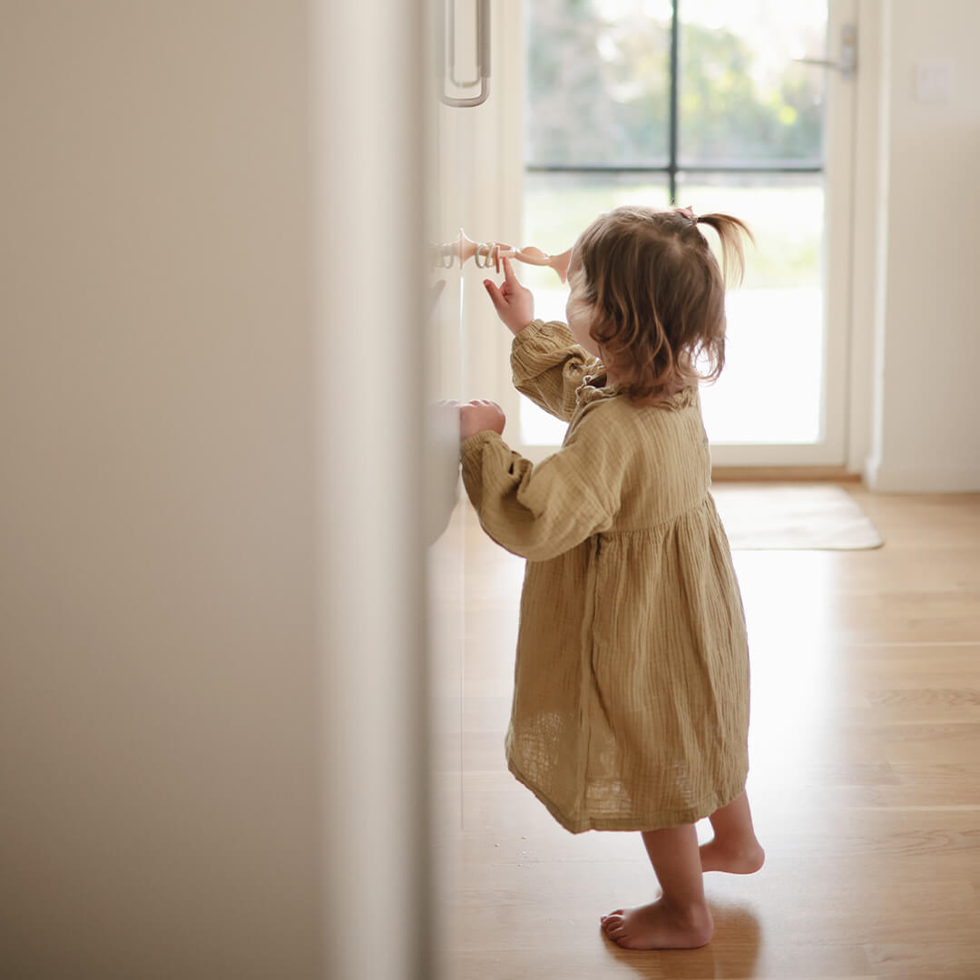 Een peuter speelt met het mushie activiteitenspeeltje dat met een zuignap aan een kast is bevestigd.