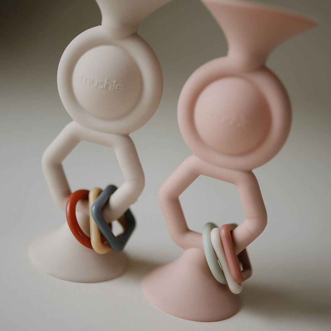 Twee Mushie activiteitenspeeltjes met zuignap in beige en roze met gekleurde ringen.