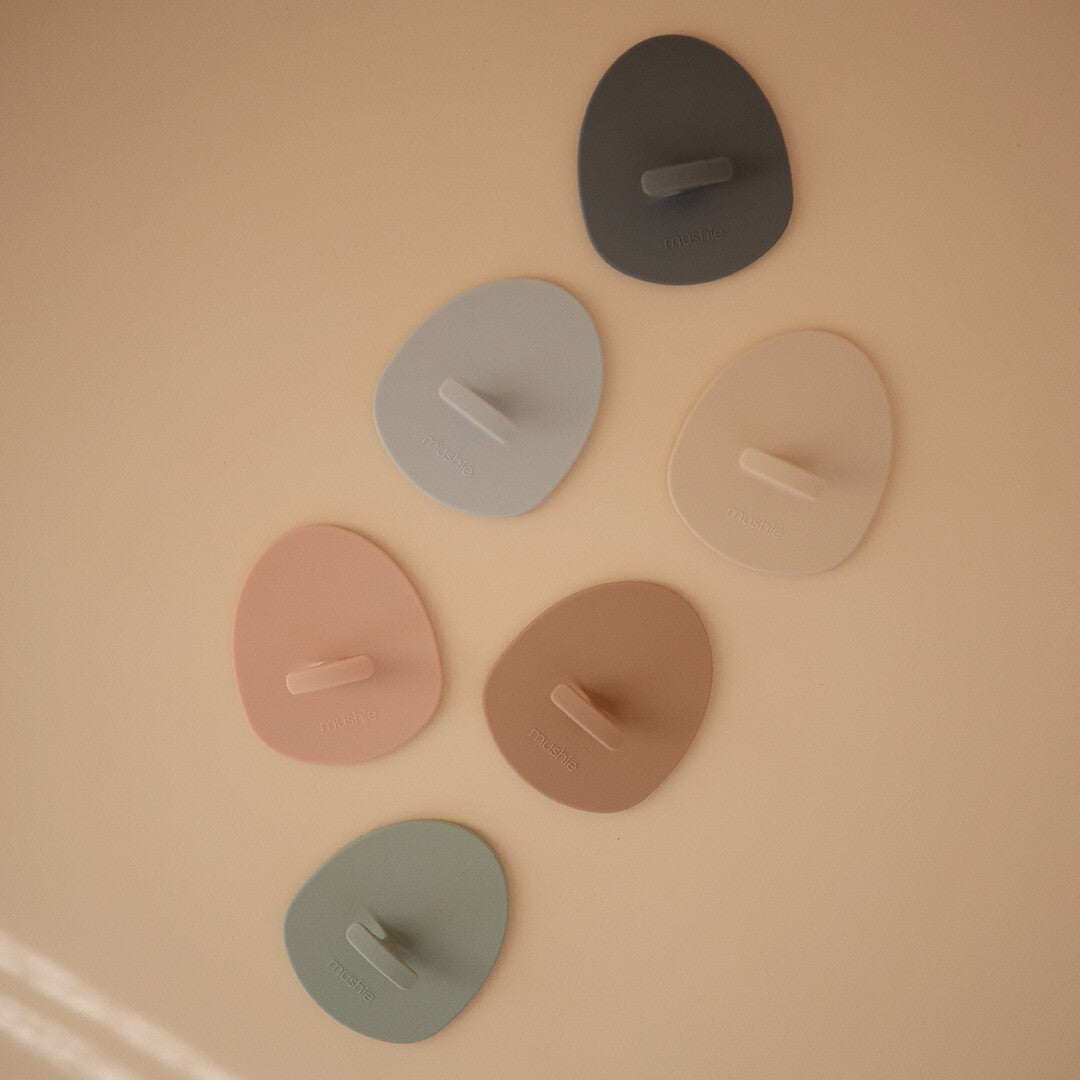 Zes mushie siliconen babyborstels in verschillende pastelkleuren liggen op een lichte ondergrond.