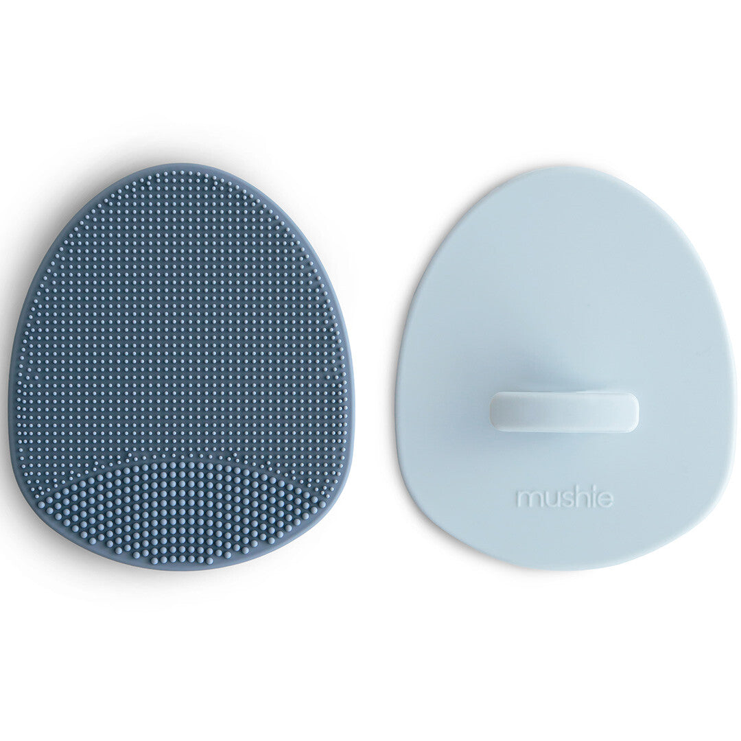 Twee mushie siliconen babyborstels, één met de borstelzijde en één met de gladde achterzijde met logo.