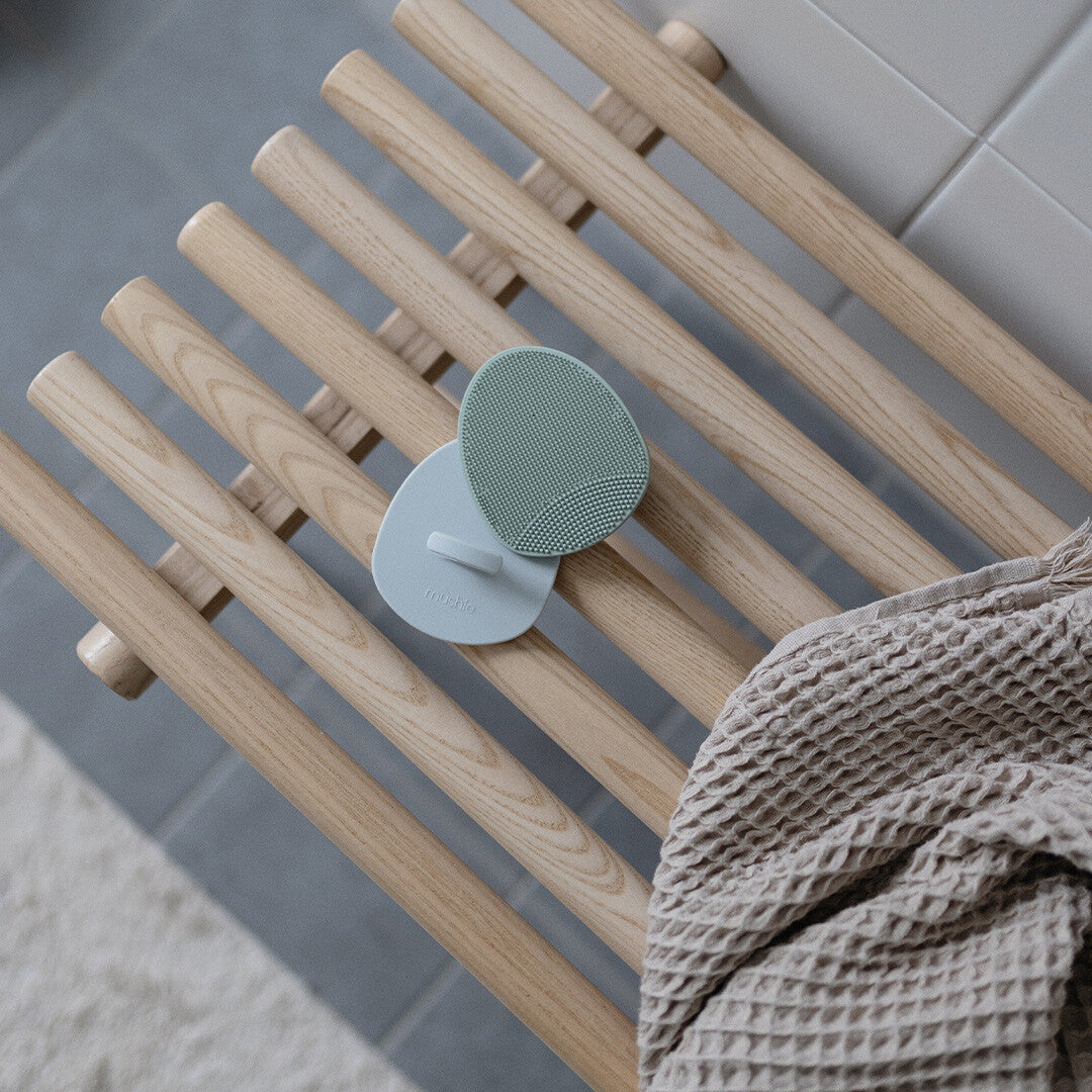 Twee mushie siliconen babyborstels liggen op een houten bankje naast een handdoek.