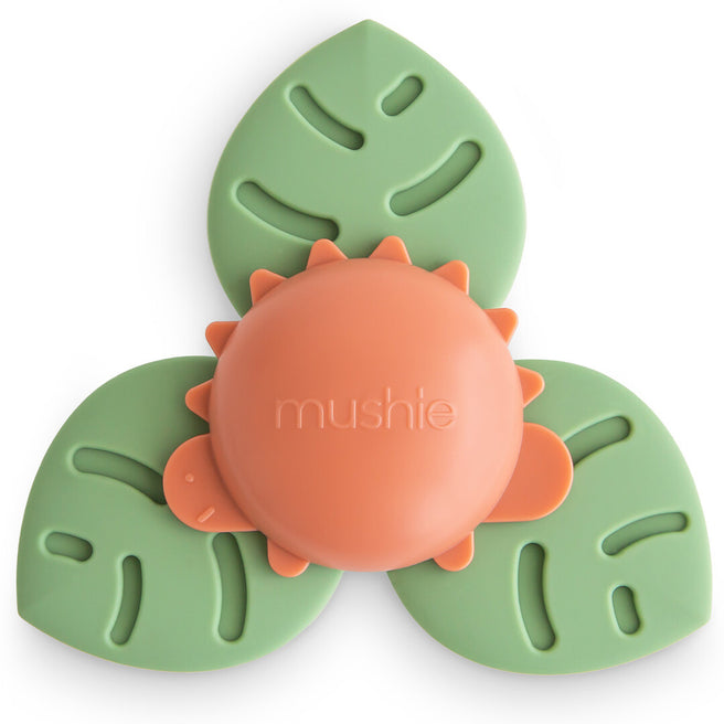 Mushie babyspeelgoed spinner met zuignap in de vorm van een oranje dino op drie groene bladeren.