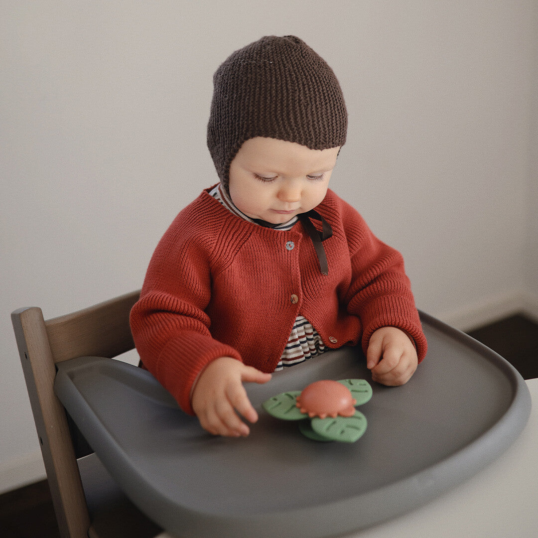 Een baby in een kinderstoel speelt met de mushie babyspeelgoed spinner met zuignap.