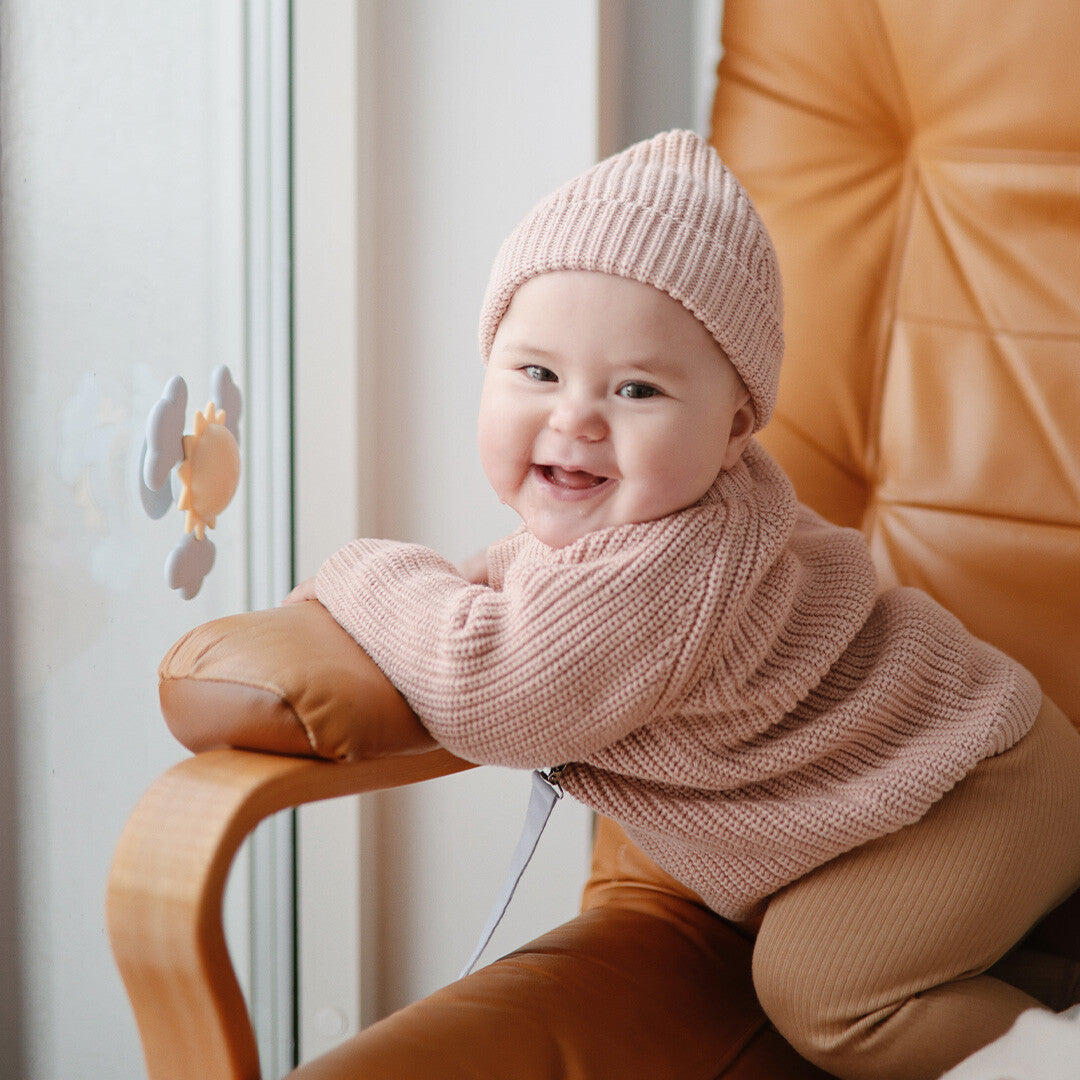 Lachende baby in een stoel kijkt naar de mushie zon- en wolken spinner met zuignap op het raam.