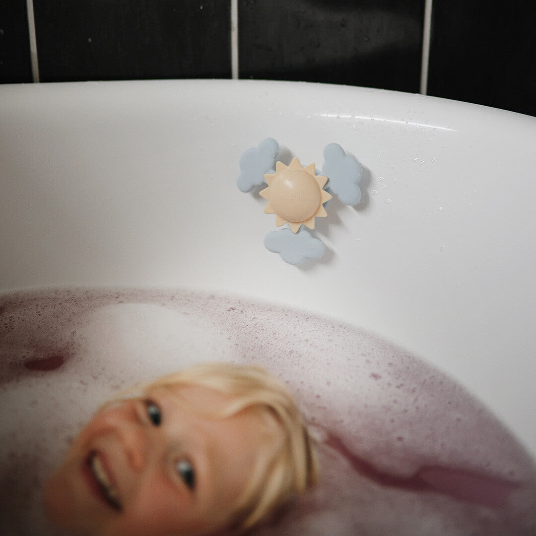 Kind lacht in een bubbelbad met de mushie zon- en wolken spinner met zuignap aan de badrand.