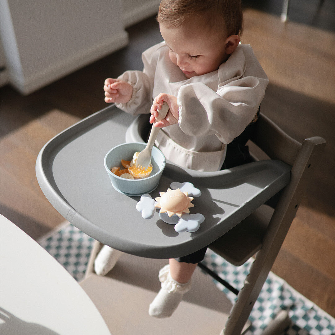 Baby in een kinderstoel met de mushie zon- en wolken spinner met zuignap op het eetblad.