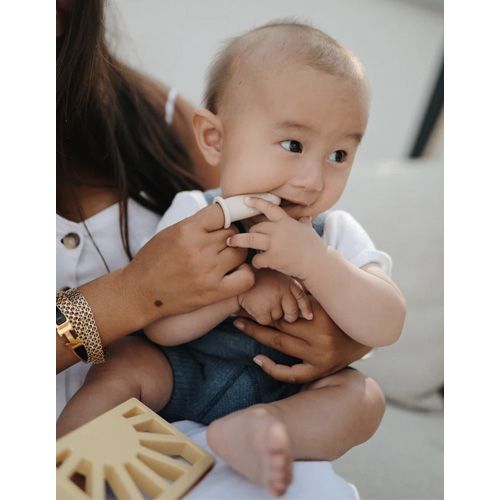 Een baby zit op schoot en kauwt op een beige siliconen babytandenborstel.