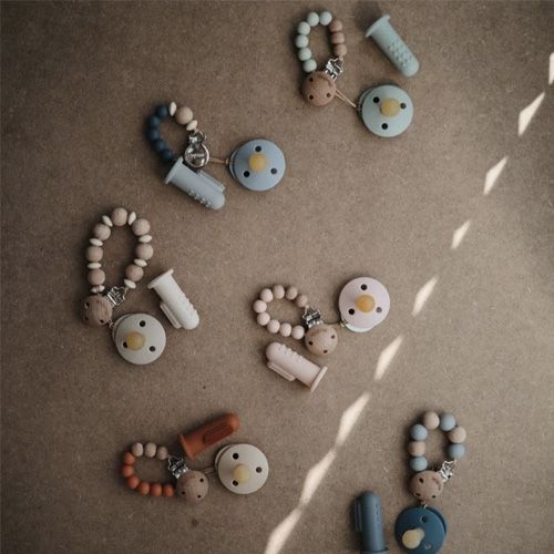 Een collectie van mushie siliconen babytandenborstels, fopspenen en fopspeenclips in diverse pastelkleuren.