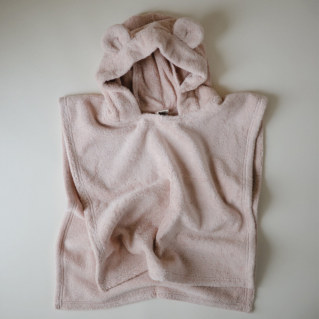 Een mushie blush roze badponcho voor baby's en peuters met berenoren, opgevouwen op een witte ondergrond.