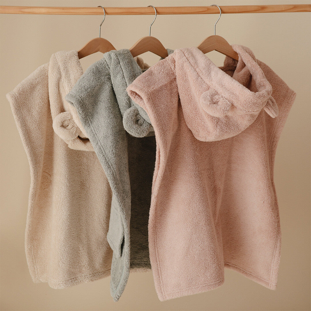 Drie mushie baby badponcho's in beige, grijs en roze met berenoortjes hangen aan houten hangers.