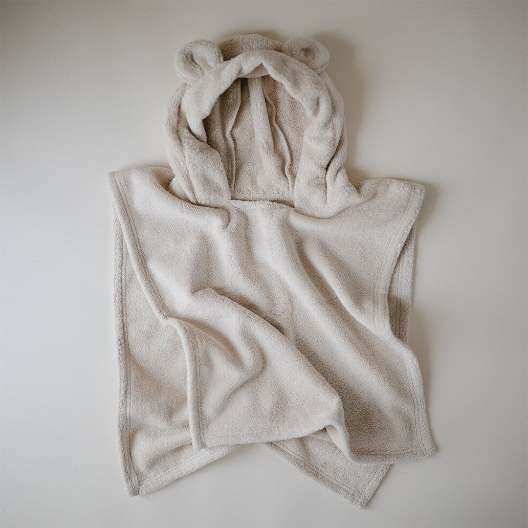 Mushie beige baby badponcho met berenoortjes, van bovenaf gezien op een lichte ondergrond.