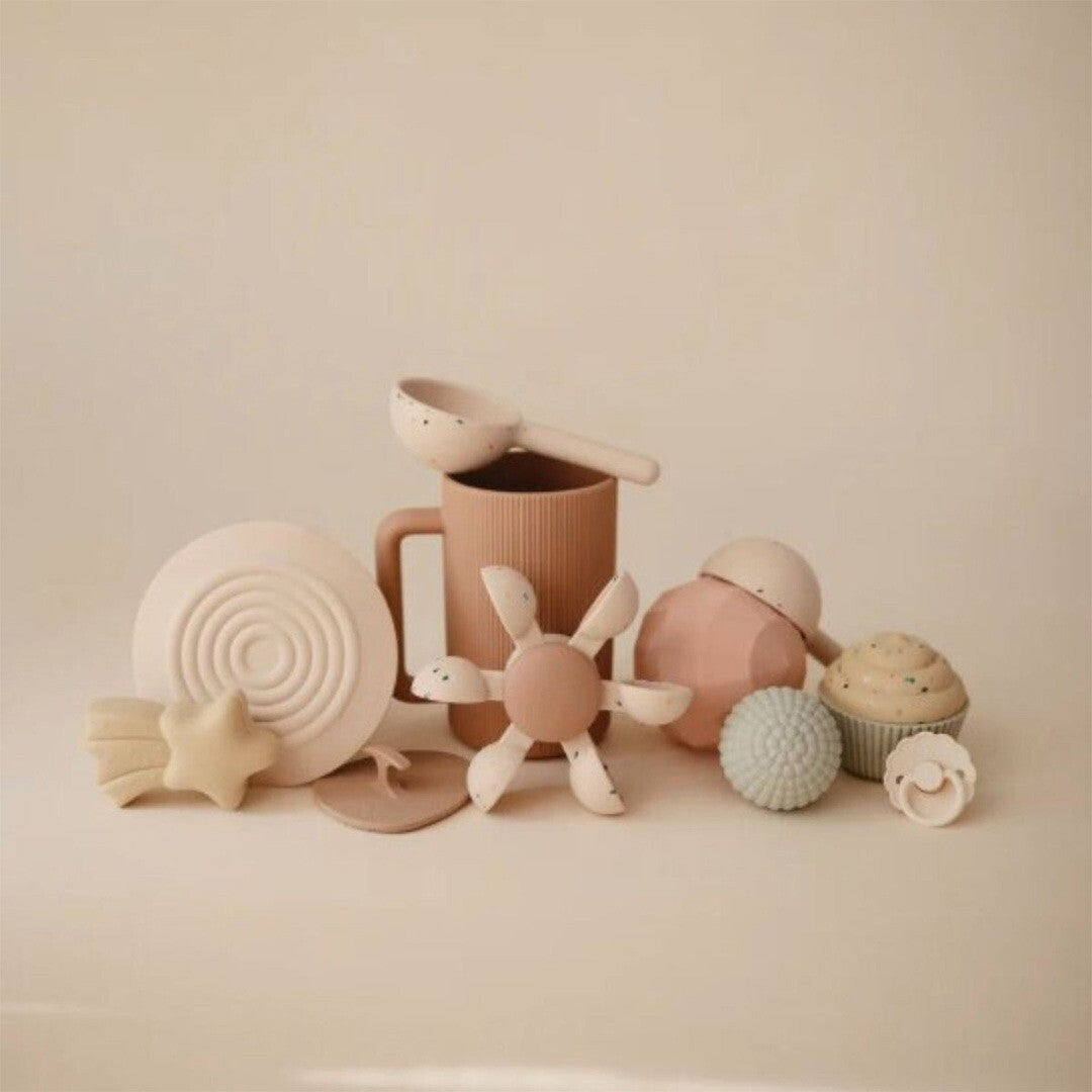 Een collectie mushie badspeelgoed in beige en lichtbruine tinten, waaronder een waterwiel, beker, ster en andere vormen.
