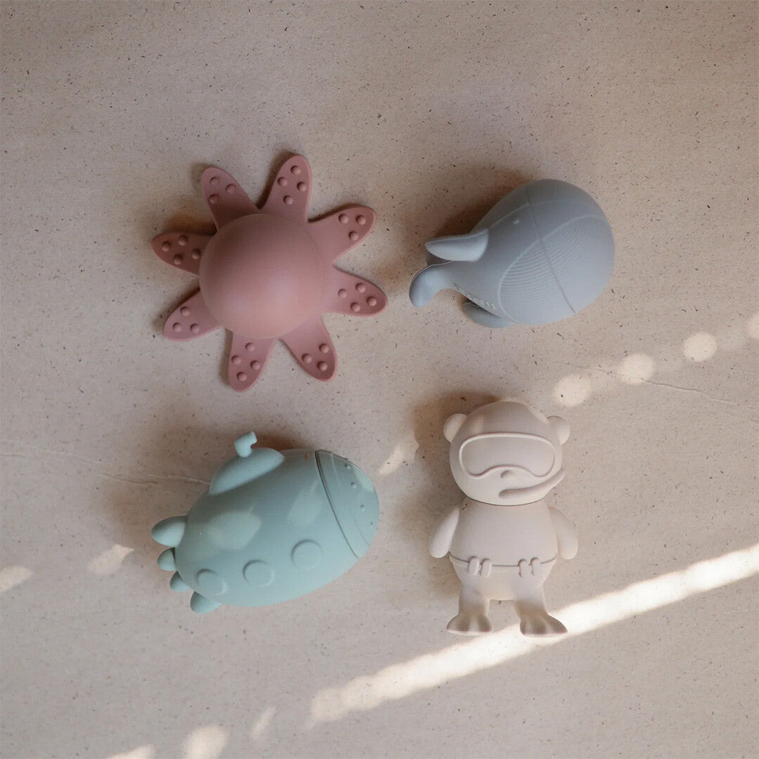 Vier mushie badspeeltjes voor baby's, waaronder een roze octopus, grijze walvis, mintgroene onderzeeër en beige beer, van bovenaf gezien.