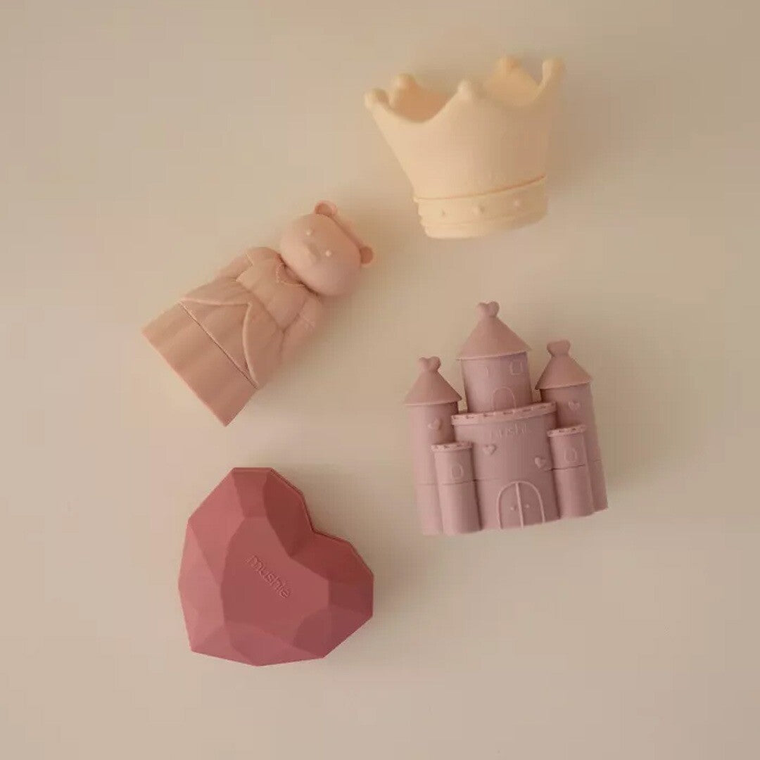 Een collectie van vier Mushie siliconen badspeeltjes: een prinsesbeer, kroon, hart en kasteel.