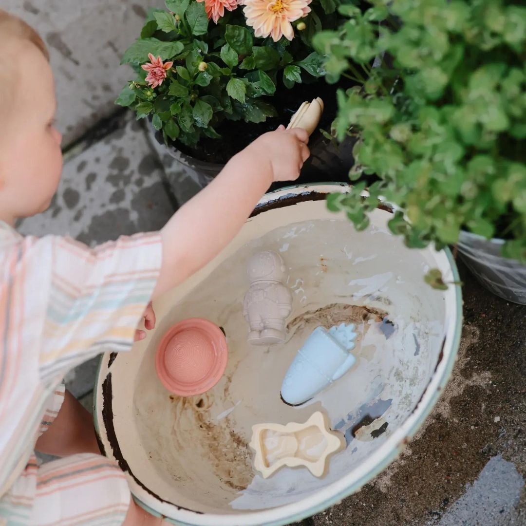 Een baby speelt buiten met de mushie ruimte badspeeltjes in een grote kom water.